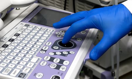 Dłoń w rękawiczce na panelu sterowania aparatu USG podczas przeglądu serwisowego