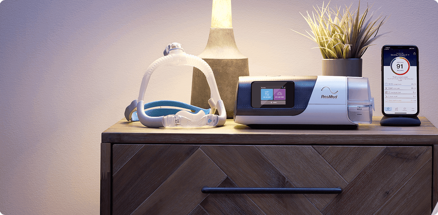 Aparat CPAP Resmed z maską i aplikacją do monitorowania terapii na szafce nocnej